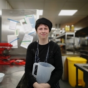 A smiling young woman holding jug in cafe kitchen